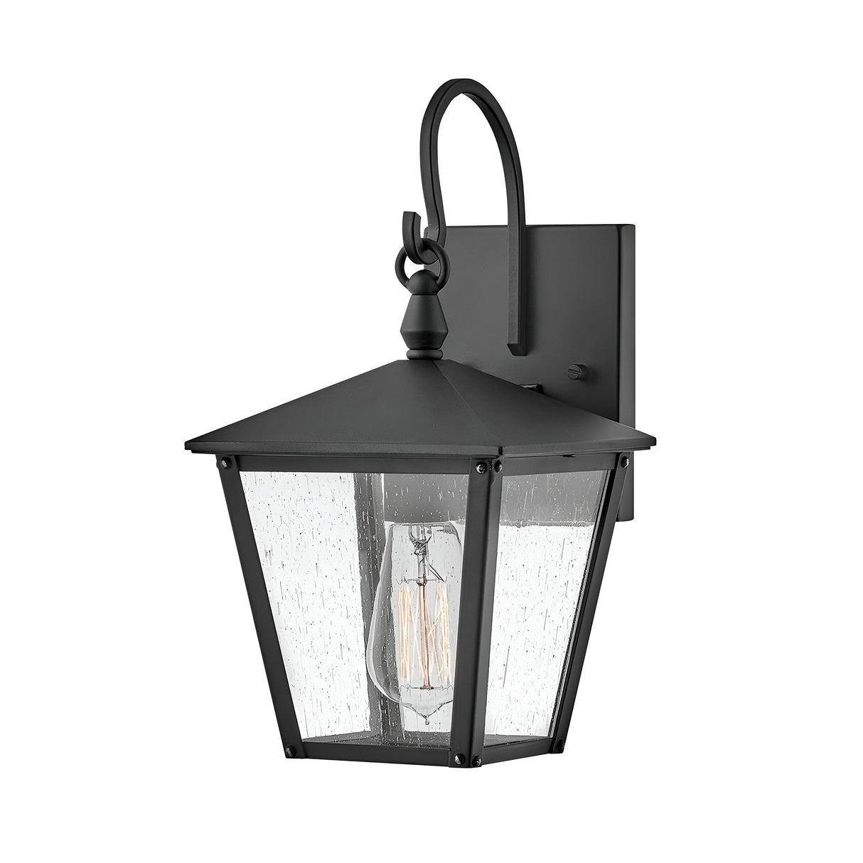 The Huntersfield Outdoor 1 Light Small Wall Lantern - Black features a black finish and clear glass shade, highlighting a visible Edison-style bulb. Its square backplate and decorative hook contribute to its classic, vintage-inspired design, perfect for enhancing any outdoor lighting scheme.