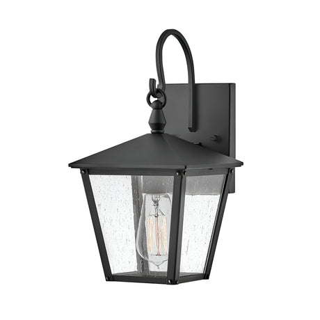 The Huntersfield Outdoor 1 Light Small Wall Lantern - Black features a black finish and clear glass shade, highlighting a visible Edison-style bulb. Its square backplate and decorative hook contribute to its classic, vintage-inspired design, perfect for enhancing any outdoor lighting scheme.