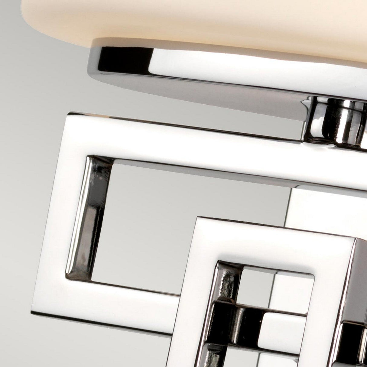 Close-up of the Lanza 1 Light Wall Light, showcasing contemporary craftsmanship with interlocking silver squares and a frosted glass element on top. The design features a sleek, polished chrome finish set against a soft gray background.