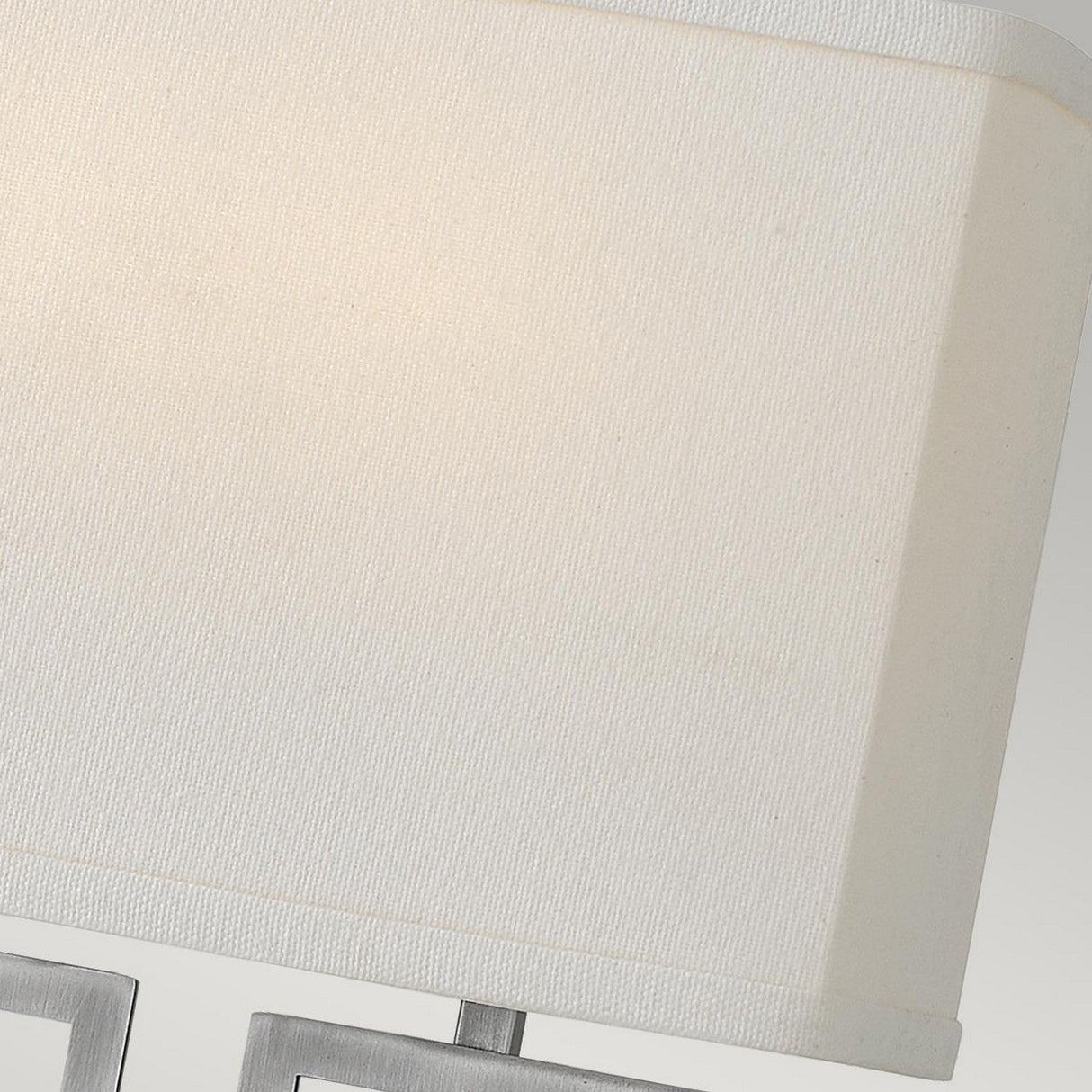 Close-up of a white fabric lampshade showcasing a subtle canvas texture, combined with the Lanza 2 Light Wall Light in Antique Nickel. The metallic frame of the lamp is partially visible at the bottom against a light gray background, perfectly complementing both modern and traditional interiors.