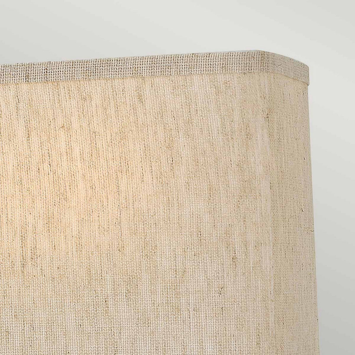 A close-up of the Lanza 2 Light Wall Light showcases its textured beige shade against a light gray backdrop. The fabric features a subtle weave pattern, enhancing its natural and earthy appeal. Complementing the minimalist design, the top edge of the rectangular shade ensures ample illumination for any space.