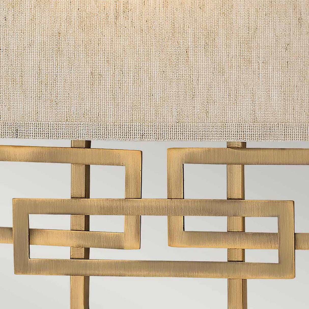 Close-up of the Lanza 2 Light Wall Light, featuring a geometric metal base in brushed bronze and a textured beige fabric shade that provides ample illumination while maintaining a minimalist and elegant design.