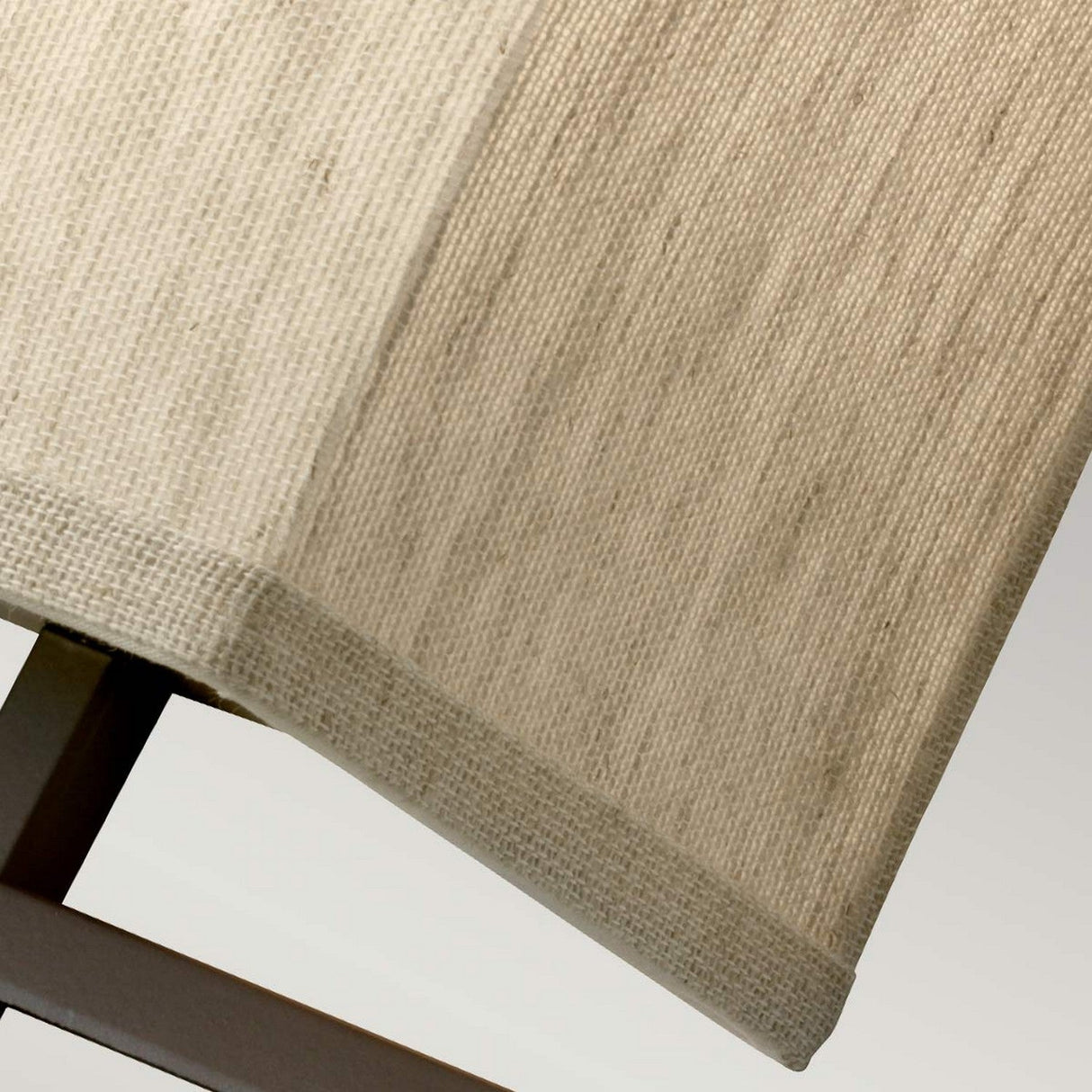 Close-up of a textured beige, rectangular-shaped lampshade ideal for modern environments. The woven fabric appearance pairs well with the partially visible oil-rubbed bronze lamp post at the base, known as the Lanza 2 Light Wall Light in Oil Rubbed Bronze. The backdrop features a gentle gradient of light hues.