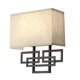 The Lanza 2 Light Wall Light in oil-rubbed bronze features a rectangular beige lampshade paired with a geometric black metal support of overlapping rectangles, infusing rustic elegance into any room. Its clean, contemporary design beautifully enhances interior decor with a stylish touch.