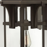 Close-up of the Manhattan Outdoor 1 Light Large Wall Lantern in an oil rubbed bronze finish, crafted from black metal and glass. Inside, a clear bulb illuminates brightly. The design features geometric shapes and clean lines, embodying a modern minimalistic aesthetic with a touch of vintage charm.