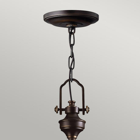 The Mayflower 3 Light Pendant - Bronze gracefully hangs from the ceiling, featuring a decorative chain and minimalist design. Its adjustable height pairs beautifully with the simple, light gray backdrop.