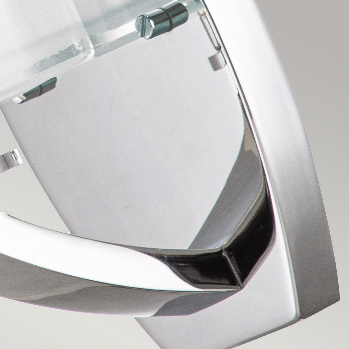 Close-up of the Meridian 1 Light Wall Light with its polished chrome finish and geometric design elements. The shiny metallic surface reflects light, accentuating its contemporary style and modern elegance against a minimalist gray background.