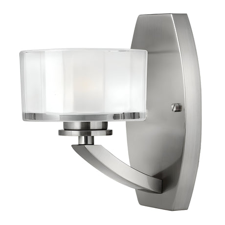 The Meridian 1 Light Wall Light in brushed nickel finish boasts a curved mount and a cylindrical frosted glass shade. Its simple, sleek design offers a contemporary look that fits well with various interior settings, making it an ideal choice for anyone looking for a stylish wall light.