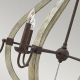 A close-up of the Middlefield 6 Light Chandelier - Iron Rust reveals a candle-shaped light bulb encased within a framework of distressed wood and metal. The iron rust finish provides an antique touch against the plain grey background.