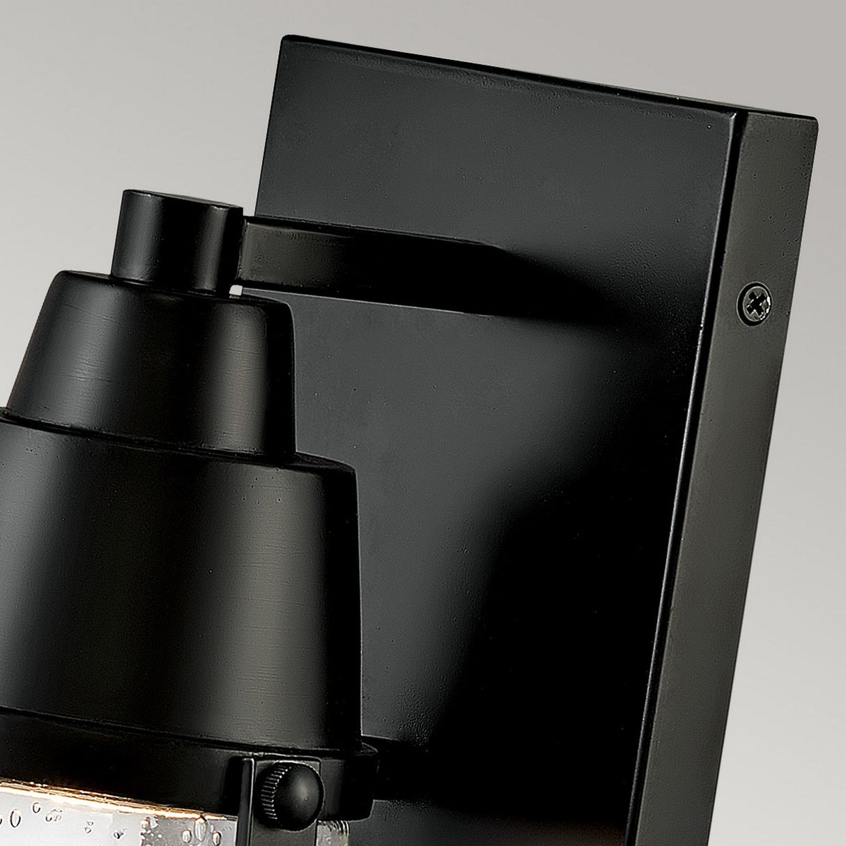 Close-up of the Miles 1 Light Wall Lantern - Black, featuring a nautical design with a matte finish and clear glass enclosure showcasing visible water droplets, mounted on a rectangular black plate against a neutral background.