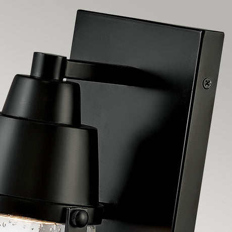 Close-up of the Miles 1 Light Wall Lantern - Black, featuring a nautical design with a matte finish and clear glass enclosure showcasing visible water droplets, mounted on a rectangular black plate against a neutral background.