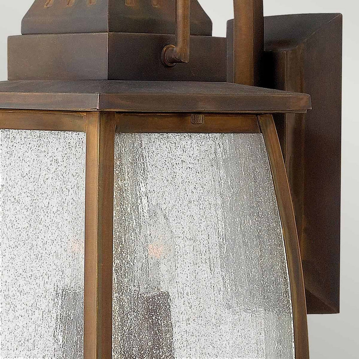 A close-up view of the rustic bronze outdoor wall lantern highlights its clear seeded glass panels and distinct Montauk 2 Light Small Wall Lantern design. The sienna-finished solid brass frame, with visible screws, enhances its vintage charm while the textured glass softly diffuses light.