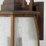 A close-up view of the rustic bronze outdoor wall lantern highlights its clear seeded glass panels and distinct Montauk 2 Light Small Wall Lantern design. The sienna-finished solid brass frame, with visible screws, enhances its vintage charm while the textured glass softly diffuses light.