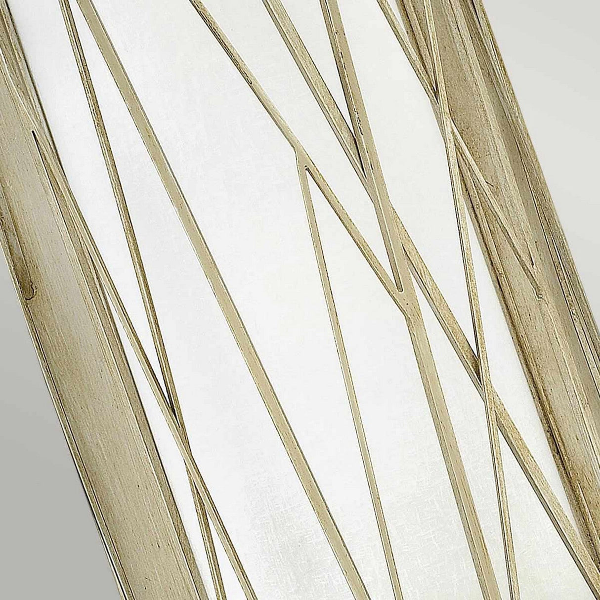 Close-up view of the Nest 1 Light Wall Light, featuring a linen glass panel accented by thin, diagonal metal lines forming an abstract geometric pattern. The metal lines have a gold finish that highlights organic modern elegance against a light gray background.