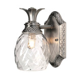 The Plantation Outdoor 1 Light Wall Light in polished antique nickel is a pineapple-shaped optic glass fixture designed for wall mounting in outdoor settings. It features a textured glass globe and metal base, casting a warm glow through its intricate pattern.