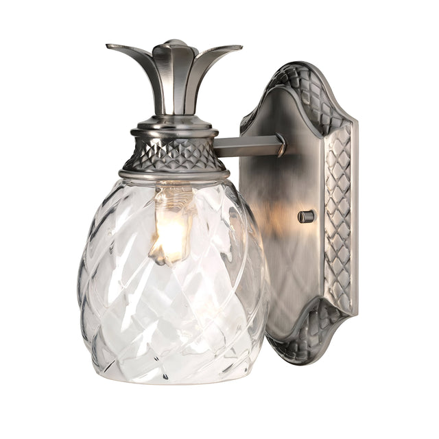 The Plantation Outdoor 1 Light Wall Light in polished antique nickel is a pineapple-shaped optic glass fixture designed for wall mounting in outdoor settings. It features a textured glass globe and metal base, casting a warm glow through its intricate pattern.