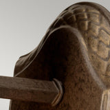 A close-up view of the vintage Plantation Outdoor 1 Light Wall Light in bronze, showcasing its intricately designed surface and curved pattern against a plain background. The focus is on its textured surface and decorative elements, highlighting the weather-resistant bronze finish.