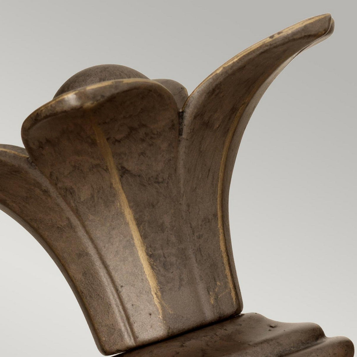 Detailed view of the Plantation Outdoor 1 Light Wall Light — Bronze, featuring an intricate crown-like design set against a plain gray background. Its surface exhibits a weather-resistant bronze finish, hinting at age or exposure to the elements.