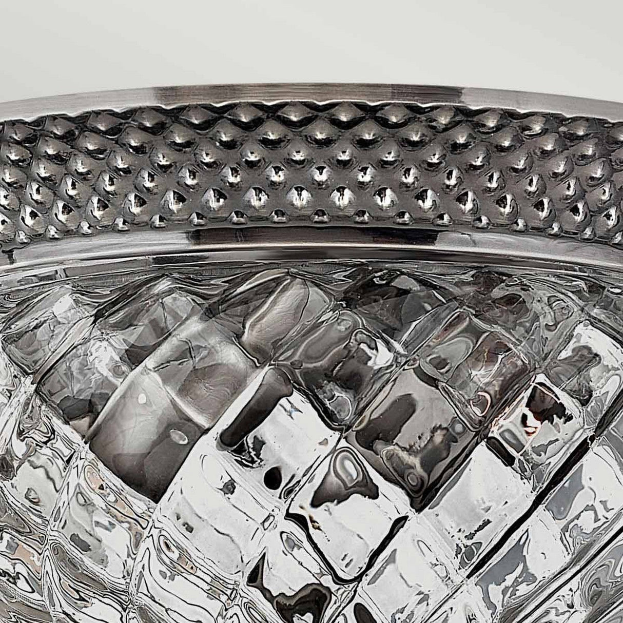 A close-up of a textured glass bowl showcases the Plantation 2 Light Small Flush in Polished Antique Nickel, featuring an optic glass design with a quilted appearance that reflects light and reveals intricate details. The metallic rim has an antique nickel finish and is adorned with a series of small raised dots.