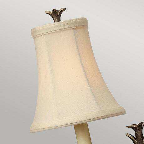 A close-up of a cream-colored lampshade features a stylized flower-shaped top finial, with the slightly flared design echoing the optic glass style seen in the Plantation 1 Light Wall Light - Bronze. The lampshade stands out beautifully against a plain background adorned with an elegant bronze finish.