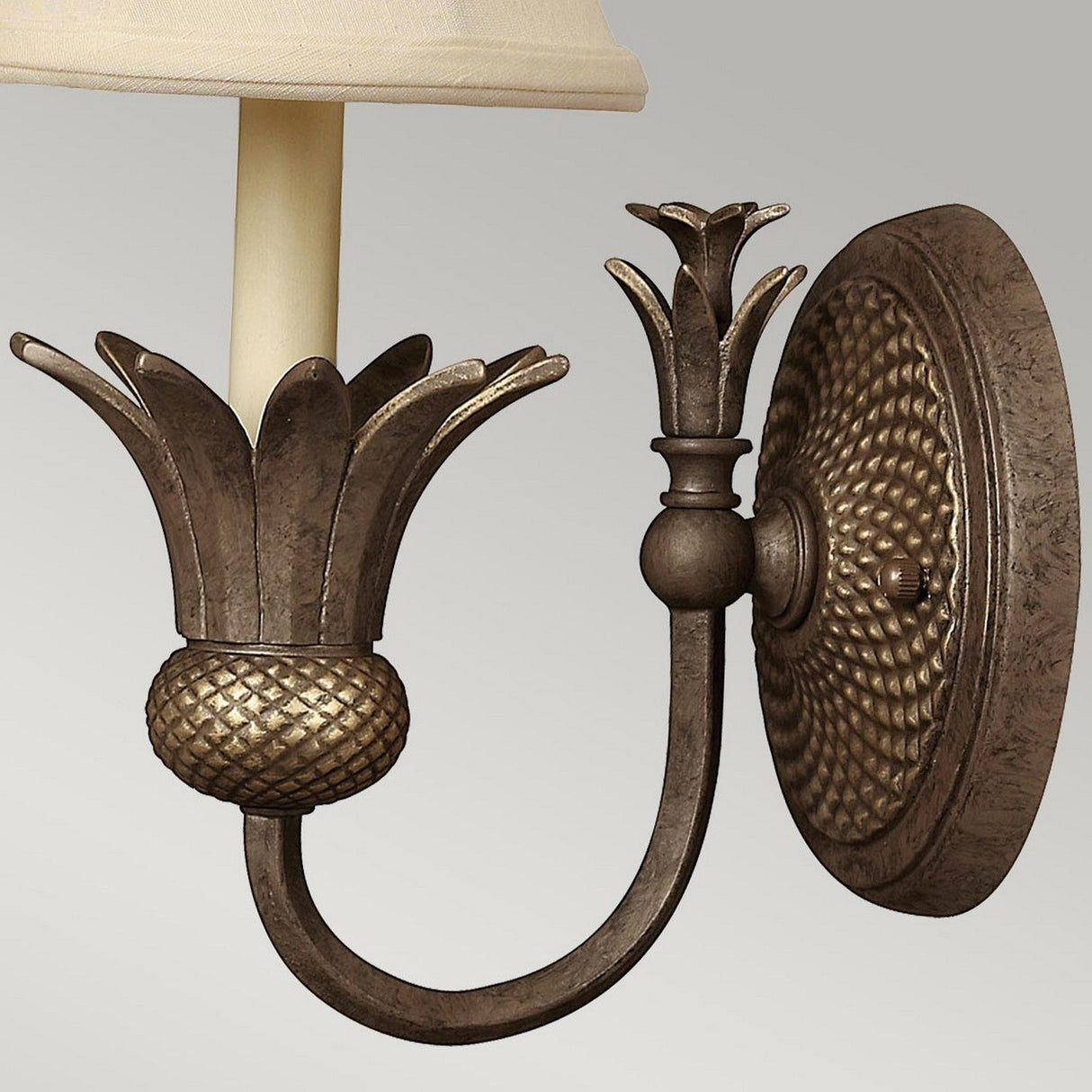 The Plantation 1 Light Wall Light - Bronze exudes vintage charm with its bronze finish and floral motif. Its ornate circular base elegantly supports a candle-shaped light holder, complete with an optic glass shade that beautifully mimics a blossoming flower bud.