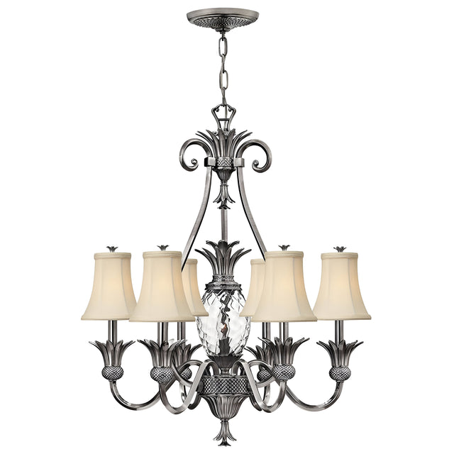 The Plantation 7 Light Chandelier in Polished Antique Nickel showcases six arms adorned with beige fabric lampshades and a central clear optic glass design shaped like a pineapple. Its detailed metalwork is elegantly suspended by a chain, making it perfect for sophisticated interior settings.