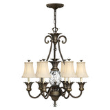 The Plantation 7 Light Chandelier in Pearl Bronze showcases intricate metalwork with seven arms, each adorned with a lamp featuring a white shade. It highlights a central pineapple-shaped clear optic glass detail, hanging gracefully from a chain.