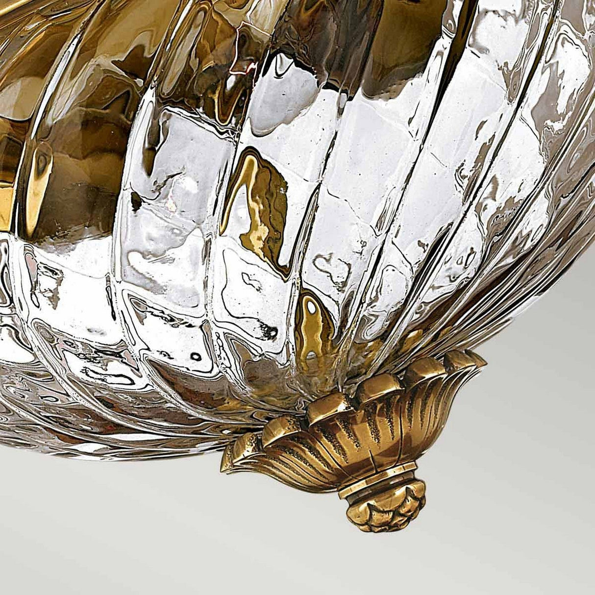 Close-up view of the Plantation 2 Light Flush with an elegant glass design and burnished brass accents. The ribbed texture of the glass creates a reflective and shiny surface, while a decorative gold base adds a touch of luxury, enhancing its sophisticated appeal.