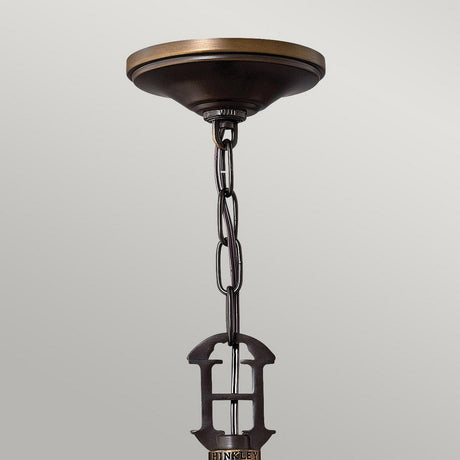 A bronze ceiling canopy with a decorative chain hangs down, showcasing a vintage-inspired large H emblem. The brand name Hinkley is engraved at the bottom of the emblem, reminiscent of the Plymouth 3 Light Chandelier - Bronze. The soft gray background enhances its timeless appeal.
