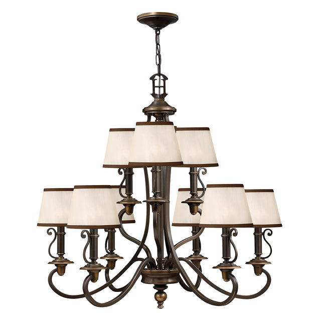 The Plymouth 9 Light Chandelier in Bronze is a large, elegant piece featuring an old bronze finish with nine cream-colored square lampshades arranged in two tiers. It boasts vintage-inspired candle sleeves, ornate curved arms, and decorative detailing, making it the perfect addition to classic or traditional interiors.