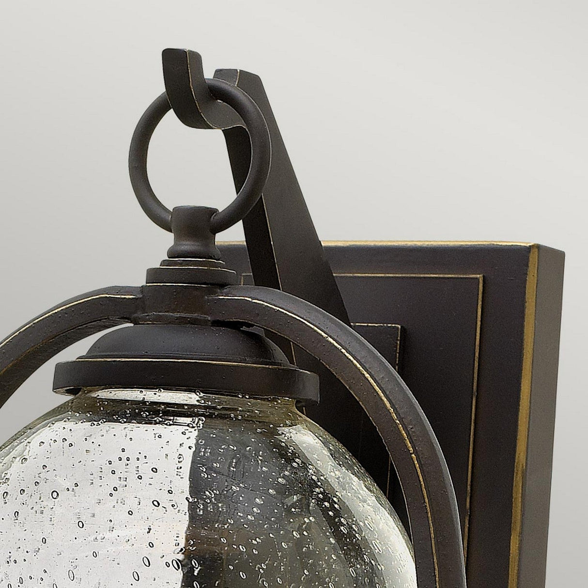 Close-up of the Quincy Outdoor 1 Light Medium Wall Lantern in Oil Rubbed Bronze, featuring a traditional design crafted from die-cast aluminum. It showcases a curved metal frame and a clear glass shade with a speckled texture, mounted on a rectangular base with decorative trim.