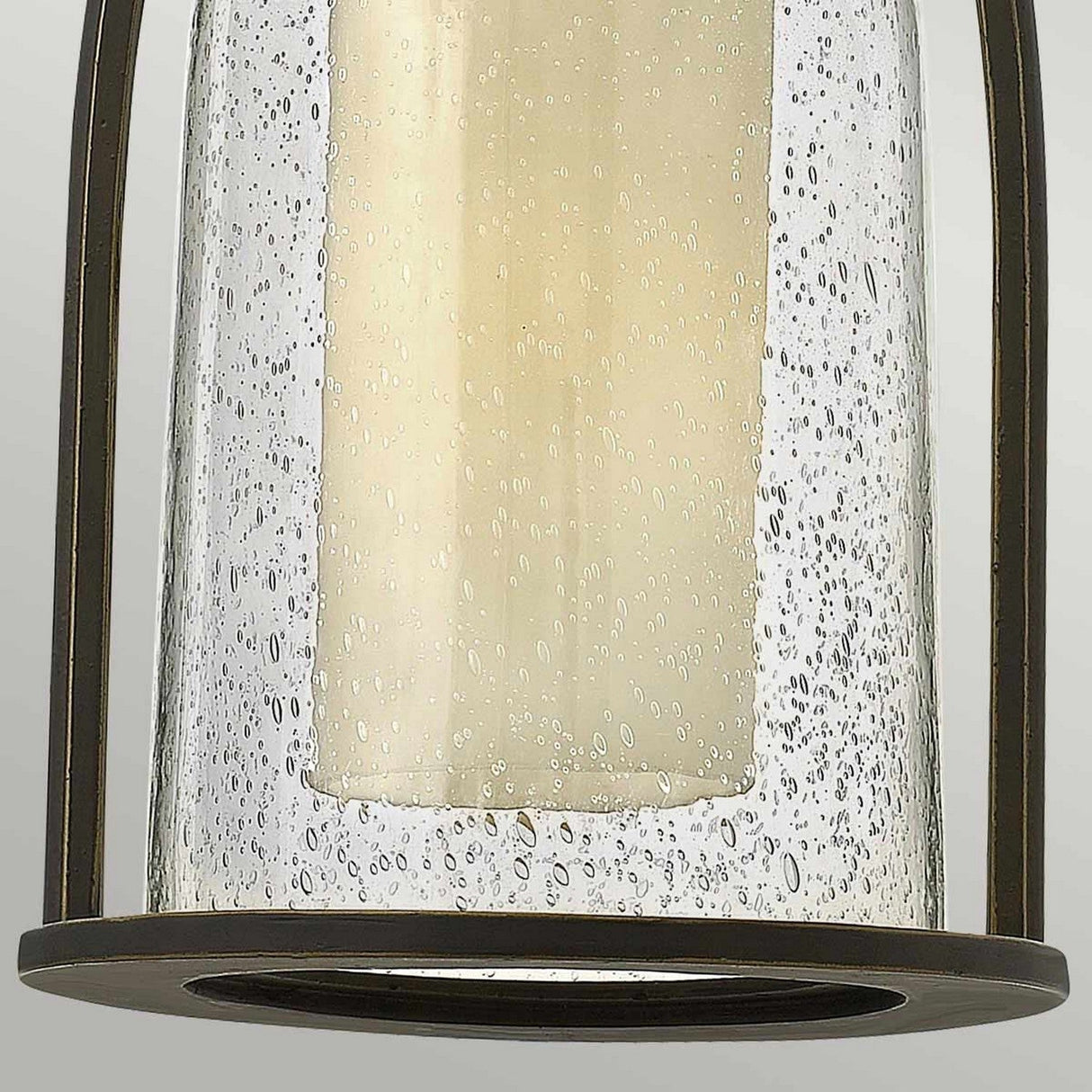 Close-up of the Quincy Outdoor 1 Light Medium Chain Pendant, showcasing its rustic design with seeded outer glass and a cylindrical cream-colored candle inside. The base and frame feature an elegant oil-rubbed bronze finish, enhancing its charm.
