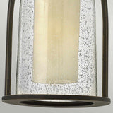 Close-up of the Quincy Outdoor 1 Light Medium Chain Pendant, showcasing its rustic design with seeded outer glass and a cylindrical cream-colored candle inside. The base and frame feature an elegant oil-rubbed bronze finish, enhancing its charm.