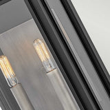 Close-up of a modern wall-mounted light fixture with two exposed Edison bulbs. The Sag Harbor Outdoor 2 Light Medium Wall Lantern - Black features a sleek black frame, adding a contemporary touch to the design.