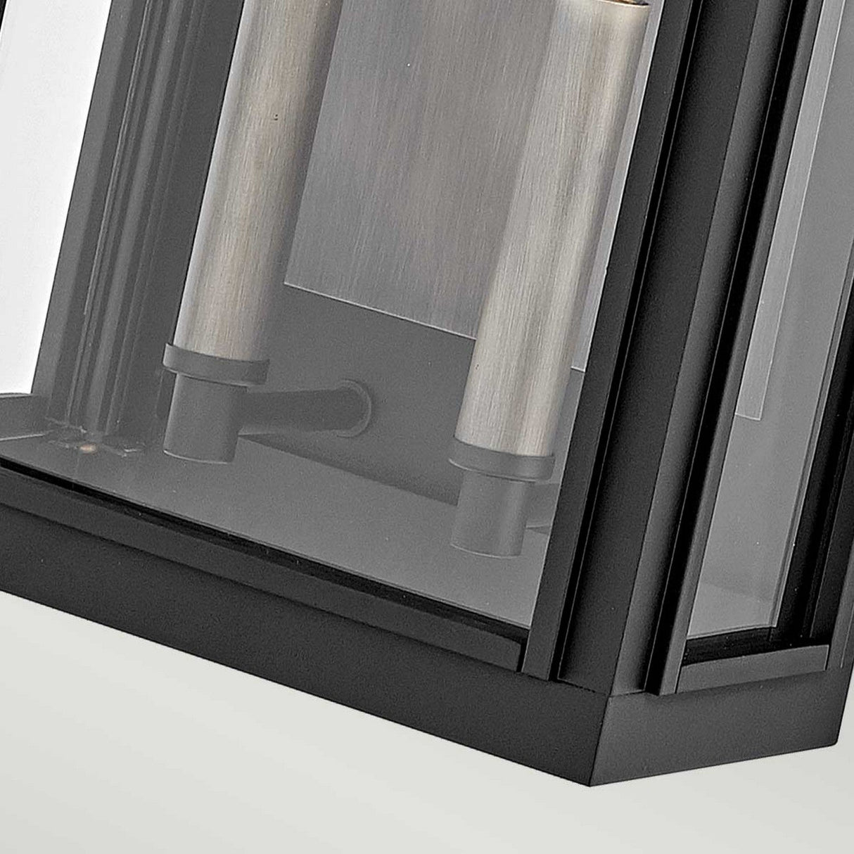 Close-up view of the Sag Harbor Outdoor 2 Light Medium Wall Lantern in black, featuring a sleek-framed glass and cylindrical lights inside. Made from durable aluminum, its contemporary metal frame makes it an ideal addition to any stylish setting.