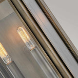Close-up of the Sag Harbor Outdoor 2 Light Medium Wall Lantern in painted burnished bronze, featuring two glowing vintage-style light bulbs encased in a rectangular metal and glass fixture. The weather-resistant lantern emits a warm glow against a neutral background, accentuating its sleek design.