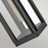 Close-up of the Sag Harbor Outdoor 1 Light Small Wall Lantern in black, highlighting its modern geometric design with a durable metal frame and clear glass panels. The IP44 rated fixture features clean, angular lines that reveal the bulb through the glass, offering an industrial aesthetic.