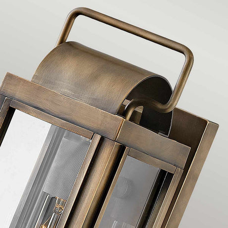 A close-up of the Sag Harbor Outdoor 1 Light Small Wall Lantern reveals its elegant blend of design, featuring a distinctive curved handle. Its painted burnished bronze finish beautifully accents the transparent glass panels, providing a clear view of the light bulb within. Combining rustic charm with practicality, this lantern is IP44 rated for reliable outdoor use.