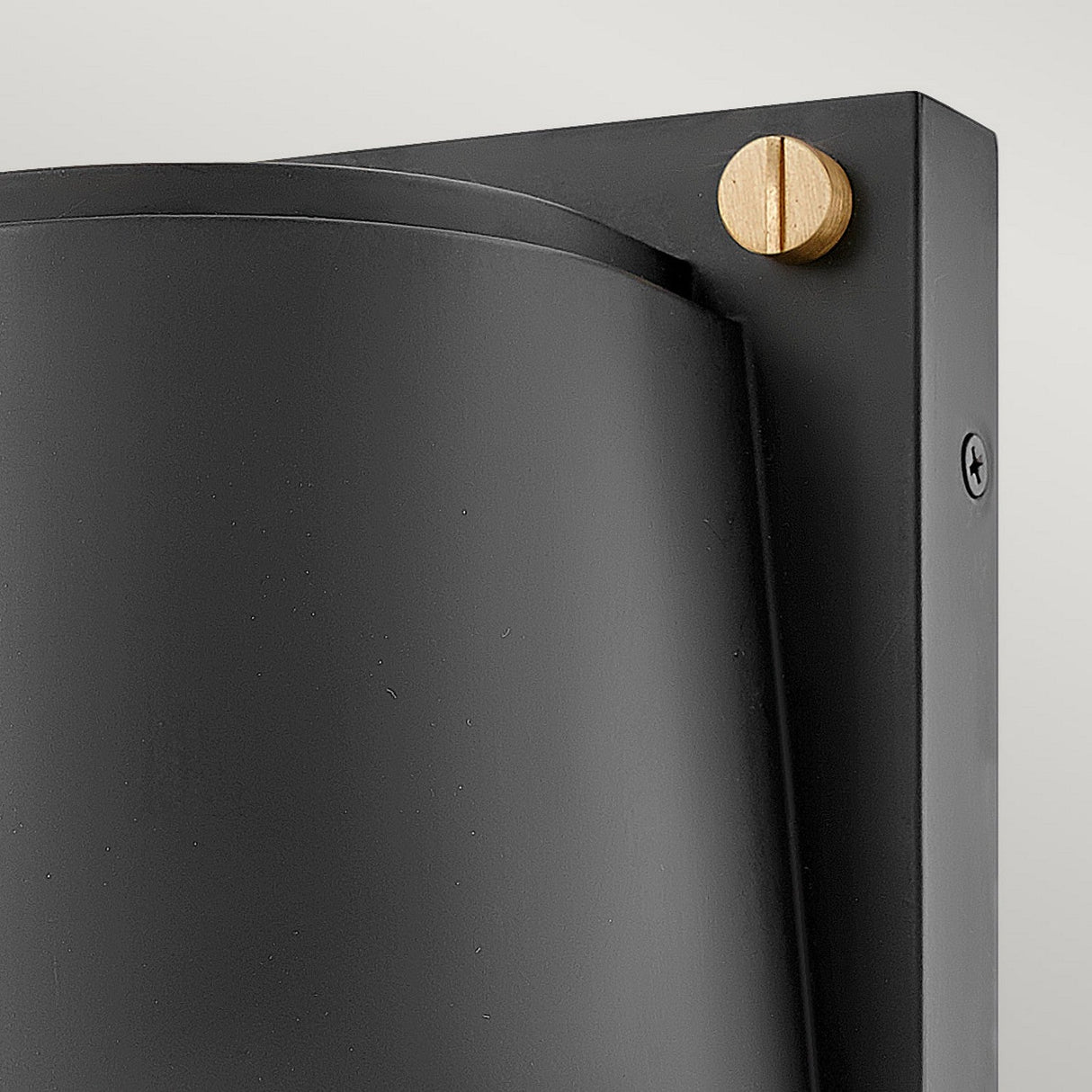 Close-up of the Scout Outdoor 1 Light Small Wall Light - Black, featuring a modern black metal structure with a weather-resistant finish and a sleek curved design. A contrasting round wooden accent is visible at the top right corner, affixed to a rectangular backplate. This minimalist outdoor wall light stands elegantly against a light background.