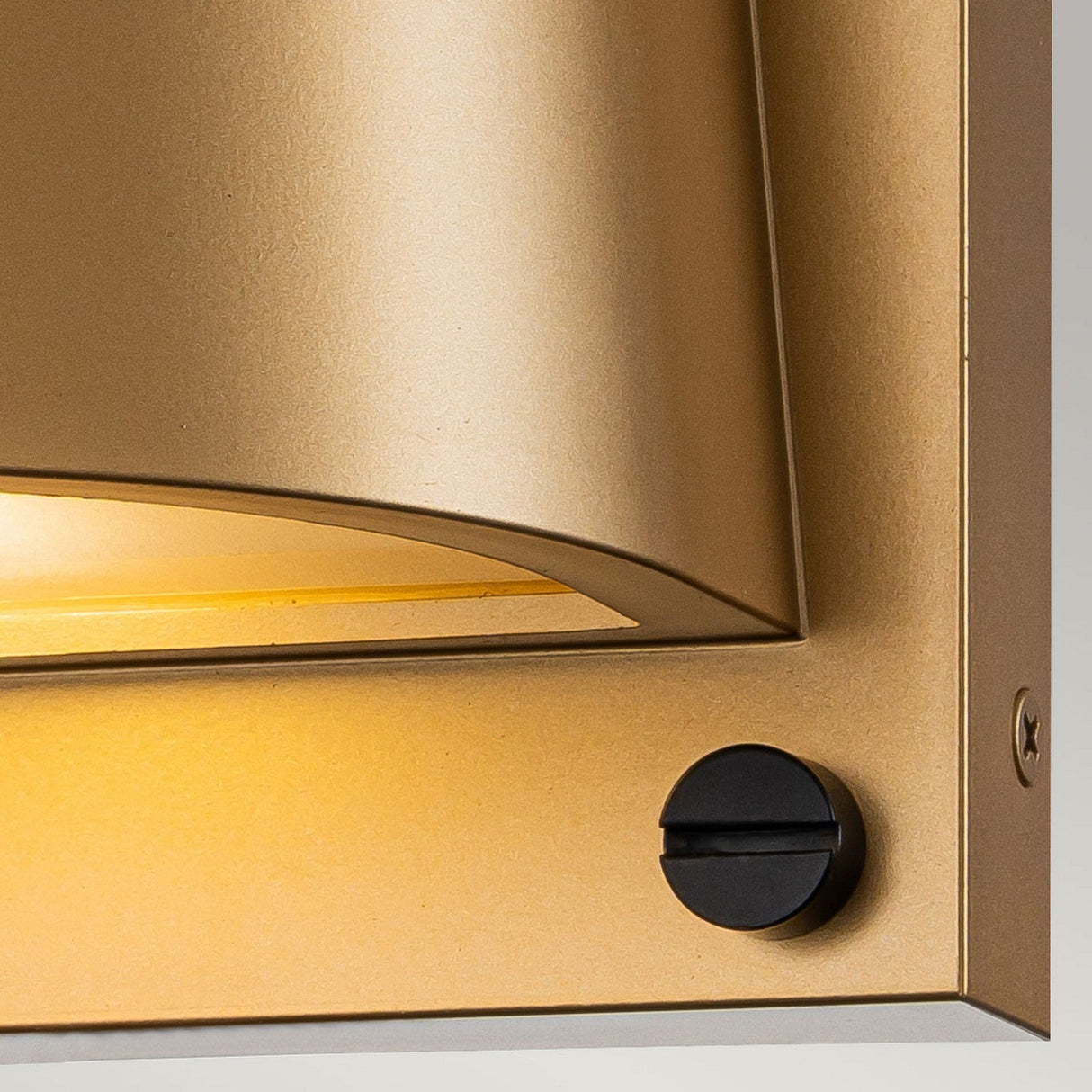 Close-up of the Scout Outdoor 1 Light Small Wall Light in painted heritage brass with a sleek, curved design. A black knob on the right side contrasts with the fixture, while warm light highlights its texture, merging elegance with functionality for impeccable outdoor lighting.