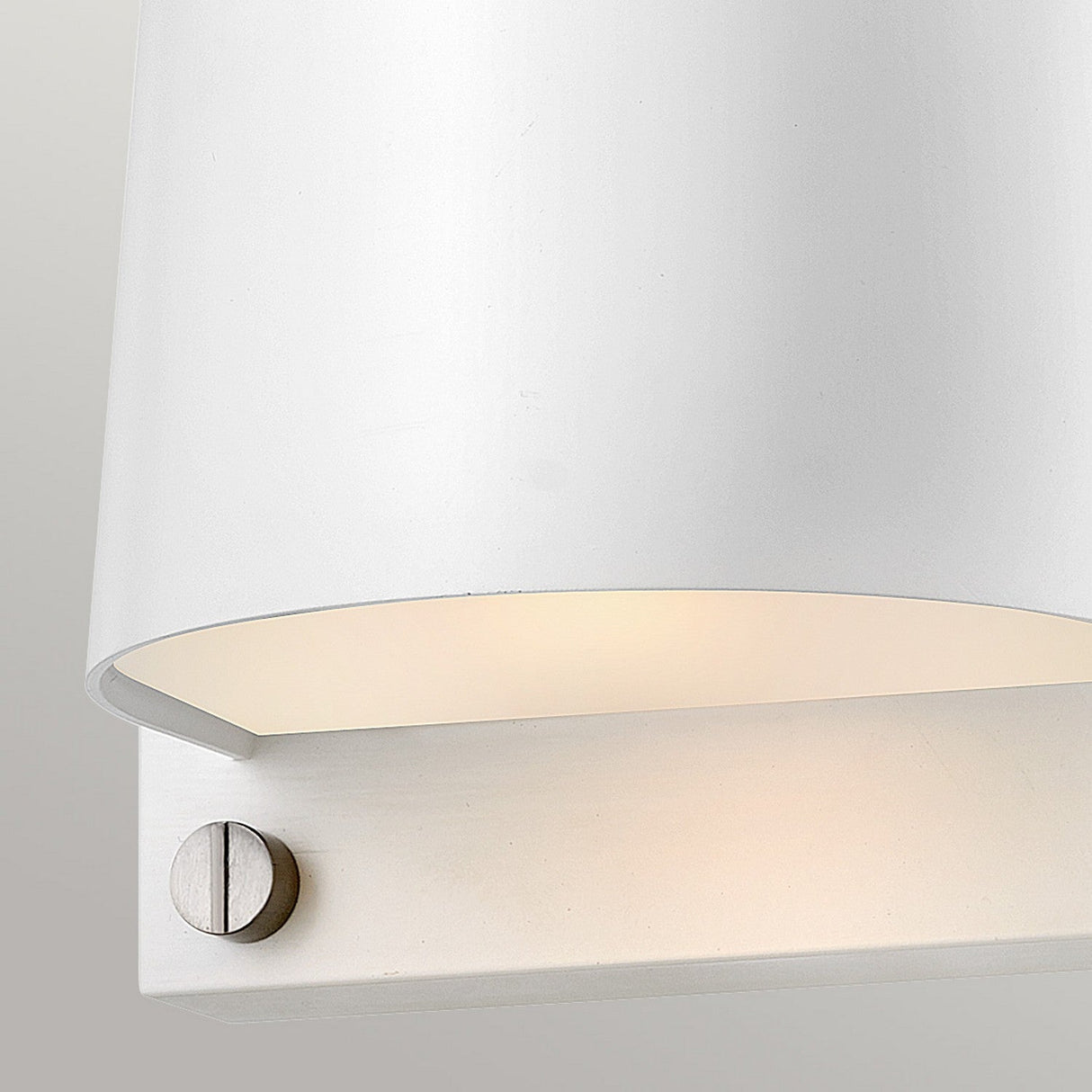 A close-up of the Scout Outdoor 1 Light Small Wall Light showcases its modern design. It has a sleek satin white finish and a cylindrical shade paired with a metallic silver base featuring a visible screw. This wall light casts soft, warm illumination from underneath, making it perfect for outdoor spaces. It's IP44 rated and elegantly stands out against the light grey background.