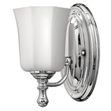 The Shelly 1 Light Wall Light in polished chrome boasts a frosted white glass shade, featuring a curved arm that connects the base to the upward-facing shade, making it a perfect fit for both traditional and modern decor.