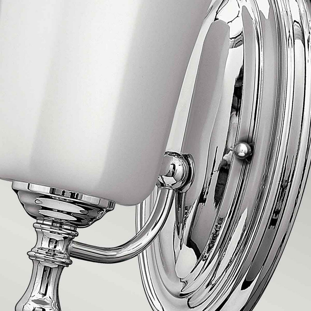 Close-up of the Shelly 1 Light Wall Light, showcasing its polished chrome finish and white, rectangular lampshade. The fixture boasts a decorative base with sleek, reflective surfaces.