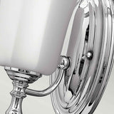 Close-up of the Shelly 1 Light Wall Light, showcasing its polished chrome finish and white, rectangular lampshade. The fixture boasts a decorative base with sleek, reflective surfaces.