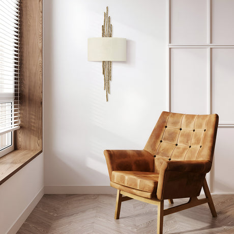 A cozy room showcases a brown leather armchair with a tufted design placed on light herringbone-patterned flooring. The Spyre 2 Light Wall Light in Champagne Gold offers accent lighting above the chair, while natural light flows in through the window on the left.