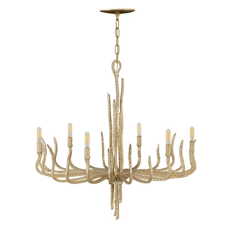 A Spyre 6 Light Chandelier in the Champagne Gold finish hangs from the ceiling with a rustic antler design. It features six light bulbs arranged in a circular pattern, emitting a warm glow. The chandelier has a natural, wood-like appearance accented with elegant Champagne Gold touches.