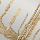 A detailed view of the Spyre 6 Light Chandelier in champagne gold reveals its curved, textured metal rods that mimic branches. The fixture's elegant and organic design is highlighted by two visible cylindrical light bulbs.