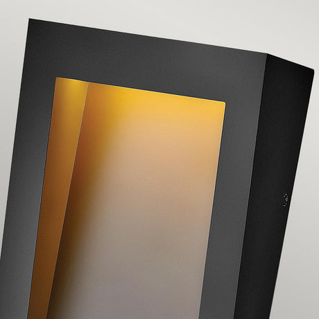 The Taper Outdoor LED Small Wall Lantern in black features a modern rectangular design with an angled opening, providing energy-efficient lighting that casts a warm yellowish glow against a light grey backdrop. This outdoor wall light serves as a chic and contemporary lighting solution for any space.