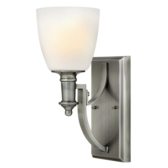 The Truman 1 Light Wall Light in an antique nickel finish features an opal glass shade, designed to accommodate a single bulb. This wall-mounted fixture offers a sleek and modern appearance with its curved arm accents and rectangular backplate.