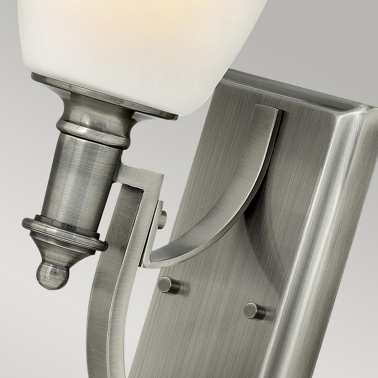 Close-up of the Truman 1 Light Wall Light in antique nickel, showcasing its opal glass shade. The sleek geometric design is enhanced by a rectangular backplate with decorative details, making it a stylish addition to any space.